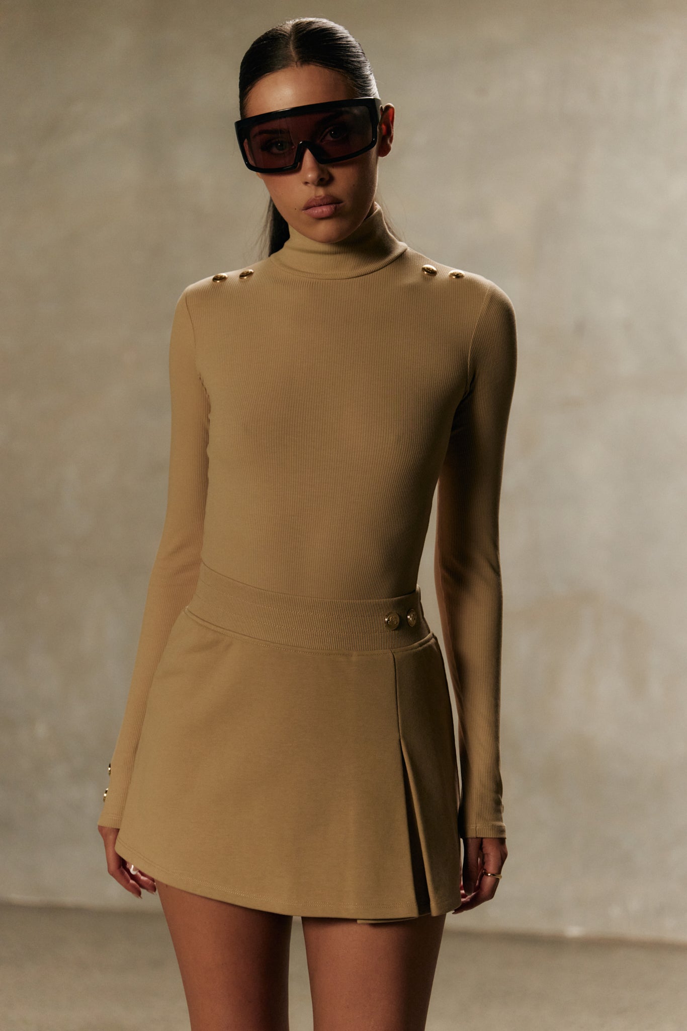 Model wearing Xaria bodysuit and xya skirt with soft pleat in desert with gold-toned signature accents 