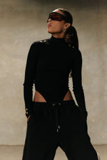 Model wearing Formation Xaria bodysuit in noir with gold-toned buttons