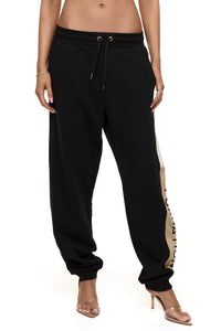 Close up of model wearing Formation noir Xion track pants with drawstring, ivory and desert contrast panels and gold-toned signature accents
