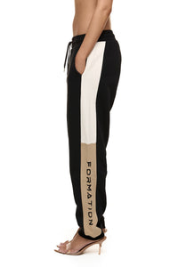 Close up of model wearing Formation noir Xion track pants with drawstring, ivory and desert contrast panels and gold-toned signature accents