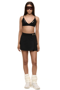 Model wearing Formation noir Xali bralette with logo embroidery and Xya Skirt in noir with soft pleat and gold-toned buttons