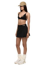 Semi side view of model wearing Formation Xali bralette with logo embroidery and Xya Skirt in noir with soft pleat and gold-toned buttons