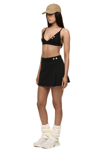Semi side view of model wearing Formation Xali bralette with logo embroidery and Xya Skirt in noir with soft pleat and gold-toned buttons