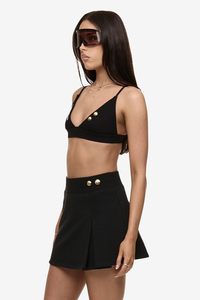 Semi side view of model wearing Formation Xya Skirt in noir with soft pleat and gold-toned buttons