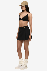 Semi side view of model wearing Formation Xali bralette with logo embroidery and Xya Skirt in noir with soft pleat and gold-toned buttons