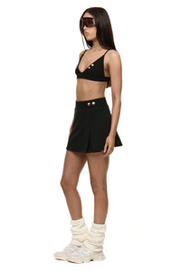Semi side view of model wearing Formation Xali bralette with logo embroidery and Xya Skirt in noir with soft pleat and gold-toned buttons