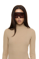 Close up of model wearing Formation Xaria bodysuit in desert side view showing gold-toned buttons