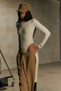 Model wearing Formation Xaria bodysuit in ivory with gold-toned buttons