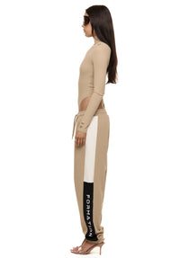 Side view of model wearing Formation Xion track pants in desert showing logo embroidery, noir and ivory side panels and gold-toned accents.