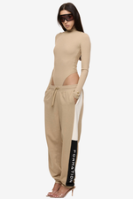 Model wearing Formation Xion desert track pants with straight leg, noir and desert side panels, gold-toned accents and embroidery logo.
