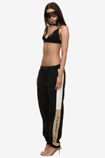 Model wearing Formation Xion noir track pants with straight leg, ivory and desert side panels, gold-toned accents and embroidery logo.