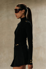 Model wearing Formation Xya Skirt in noir, side view showing soft pleat and gold-toned buttons